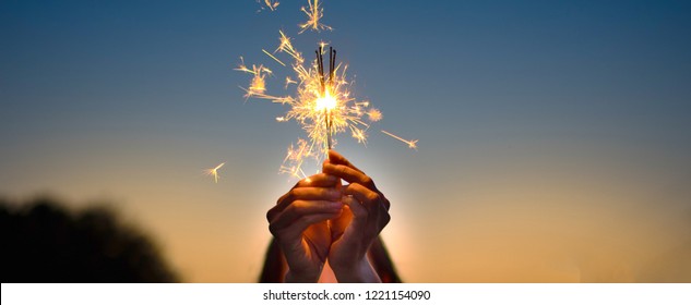 Abstract blur sparklers for celebration background,Motion by wind blurred woman hand holding burning Christmas sparkle on nature and twillight sky background.Winter vintage film grain filter style. - Powered by Shutterstock