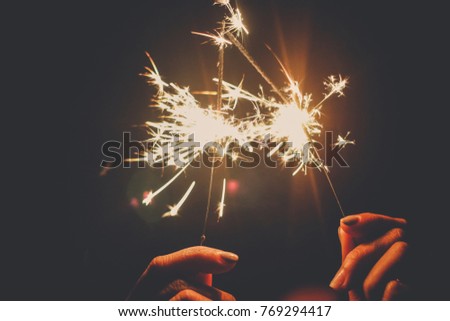 Abstract blur sparklers for celebration background,woman hand holding a burning sparkler light with purple sky background.closeup in female hand in dark. happy holidays.Vintage flim grain Style.