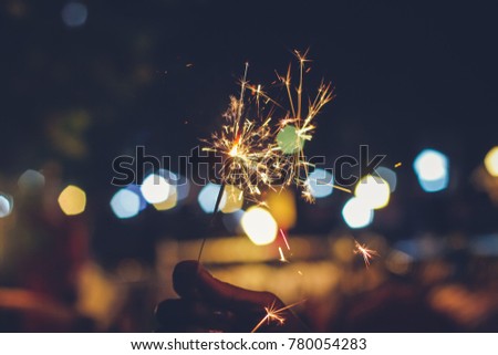 Abstract blur sparklers for celebration christmas,festival and party background,Motion Blurred Sparklers in woman hand holding at Market Street City with bokeh.Winter Dark vintage film grain style.