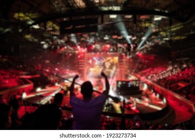 Abstract blurred background of big esports gaming event at big arena. Man with a hands raised.