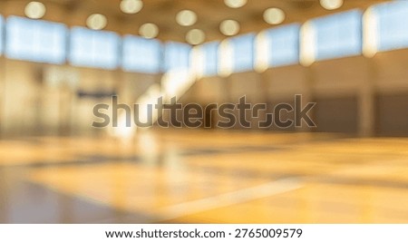 Abstract blurred background of an empty indoor sports hall with a wooden floor and bright overhead lights, creating a warm and inviting atmosphere suitable for various athletic activities.