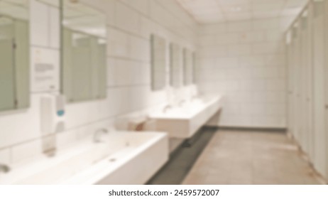 Abstract blurred background of interior public toilet and restroom in a Shopping Mall. Empty public toilets with white sinks, wide wall mirror and WC stalls. Concept for clean public washroom design.