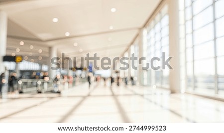 Abstract blurred background of a spacious and bright airport terminal interior. Large windows let in natural light, with silhouettes of people walking in the distance.