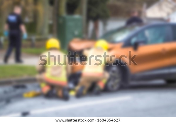 Abstract blurred fire\
service firemen examining a crashed car in the street after a road\
traffic accident.