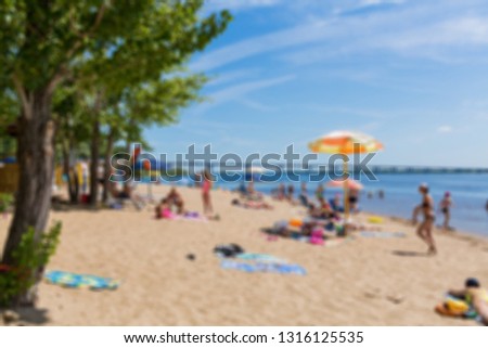 Abstract blurred image. Defocused lens, bokeh. People sunbathe and swim in the river on a sandy beach. On a Sunny summer day. Road bridge on the horizon.