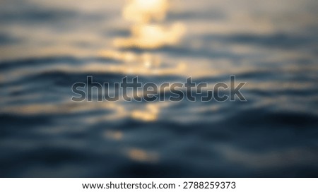 Abstract blurred image of ocean waves reflecting golden sunlight during sunset, creating a tranquil waterscape scene. The soft focus enhances the serene atmosphere.