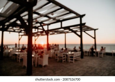 Abstract Blurred Image Of Outdoor Restaurant Terrace On Warm Summer Evening Sunset Over The Sea With Bokeh For Background. Holiday, Vacation And Travel Concept