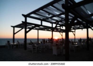 Abstract Blurred Image Of Outdoor Restaurant Terrace On Warm Summer Evening Sunset Over The Sea With Bokeh For Background. Holiday, Vacation And Travel Concept