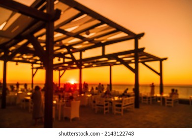 Abstract Blurred Image Of Outdoor Restaurant Terrace On Warm Summer Evening Sunset Over The Sea With Bokeh For Background. Holiday, Vacation And Travel Concept