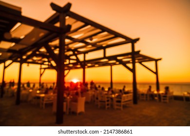 Abstract Blurred Image Of Outdoor Restaurant Terrace On Warm Summer Evening Sunset Over The Sea With Bokeh For Background. Holiday, Vacation And Travel Concept