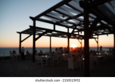 Abstract Blurred Image Of Outdoor Restaurant Terrace On Warm Summer Evening Sunset Over The Sea With Bokeh For Background. Holiday, Vacation And Travel Concept