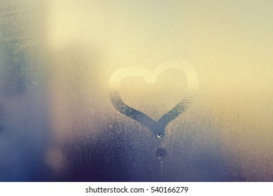 Abstract blurred love heart symbol drawn by hand on the wet frozen door window glass with sunlight background. Closeup of emotional image - Shutterstock ID 540166279
