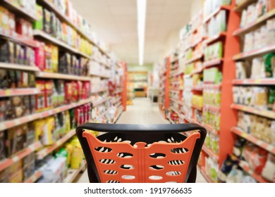 Abstract blurred photo of supermarket with empty shopping cart near packages on shelves in store. Trolley in supermarket and blur product on background.