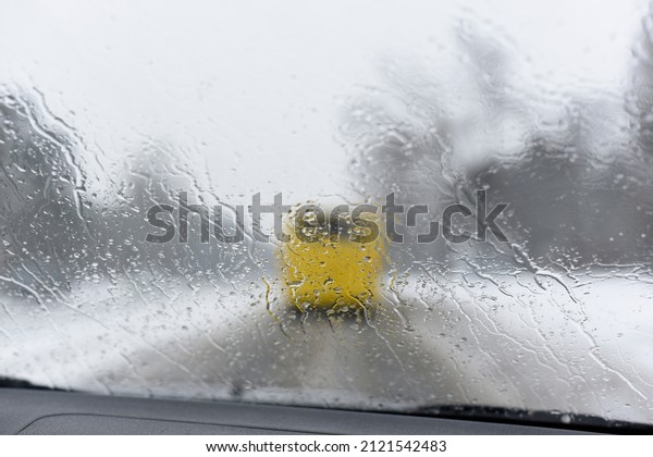 Abstract blurred yellow bus at snowy and rainy day.\
Road through the wet windshield of the car. Conceptual bad weather\
background. Traffic view from car windscreen in rain. Driving in\
rain.