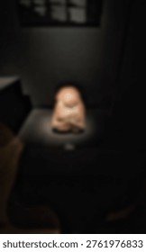 An abstract, blurry ancient object is dramatically spotlit in a dark museum or gallery exhibit.