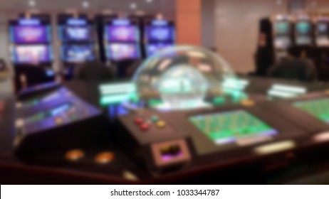 Abstract Blurry Background With Gambliing Room, Roulette On Table, Poker Table And Slot Machine, No People In Image