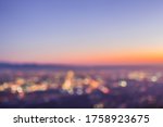 An abstract blurry image of a city skyline at sunset, featuring round bokeh balls from the twinkling lights below. View from Potato Mountain in Claremont Wilderness Park near Los Angeles California