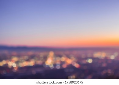 An abstract blurry image of a city skyline at sunset, featuring round bokeh balls from the twinkling lights below. View from Potato Mountain in Claremont Wilderness Park near Los Angeles California