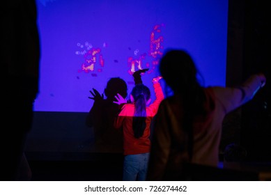 Abstract, Blurry New Technology Background. Little Girl Is Playing With Interactive Visual Installation Projected On Wall