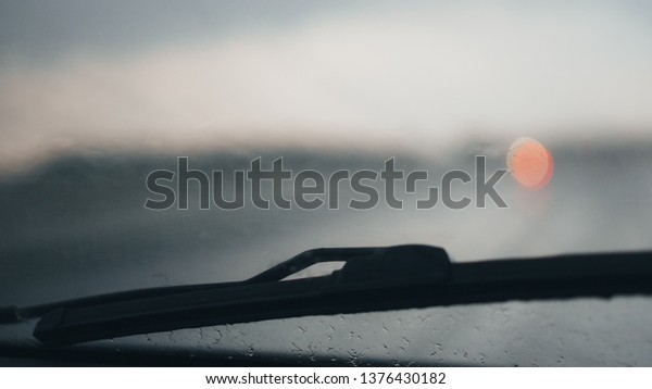 Abstract car window in raining day. View from\
car seat. Blur Background at sunset. Drops of rain on car window\
pane. Blurred droplet on car window. Wiper glass raindrops. Driving\
in rain weather.