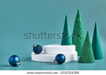 Abstract christmas composition template for exhibition beauty product. Geometric Paper Christmas trees near white gypsum pedestal and blue christmas balls on turquoise pastel background. Winter sale.