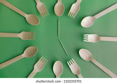 Abstract clock made from disposable wooden cutlery (forks, spoons and toothpicks as clock hands) lying on green background. 5 o'clock - time to drink tea. Environmental protection theme.