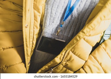 An Abstract Close Up Of A Blank Black Lanyard Around The Neck Of A Person Wearing A Mustard Yellow Jacket, And Grey Jumper. Nice Depth Of Field To Emphasis The Lanyard. On A Blue Neck Strap. 