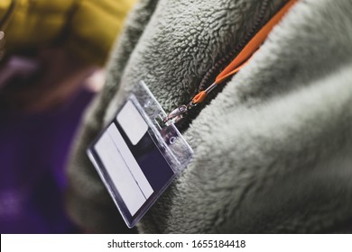 An Abstract Close Up Of A Blank Lanyard Around The Neck Of A Woman Wearing A Grey Fur Jacket. Nice Depth Of Field To Emphasis The Lanyard. On A Orange Neck Strap. 