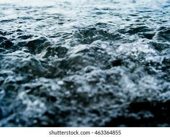 Abstract close up and selective focus shot of water surface with flow waves and bubbles.