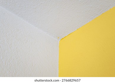 Abstract close up of a sharp corner where a vibrant yellow wall meets a white plaster ceiling