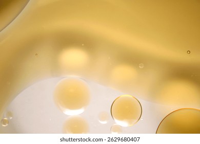 An abstract close-up image showcasing the interplay of oil and water with soft golden highlights and glowing bubbles. Ideal for artistic design projects.