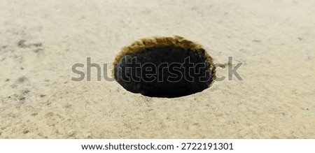 Abstract close-up macro of a dark circular hole in rough textured light beige industrial material surface background, detailed pattern view. 