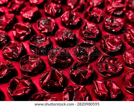 Abstract close-up of metallic red bubble wrap texture with glossy reflective surface, creating a vibrant geometric background.