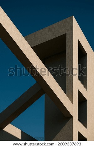 Abstract close-up of modern architectural elements with intersecting concrete planes and dramatic triangular shadow. Captured in natural daylight against a blue sky, this image highlights