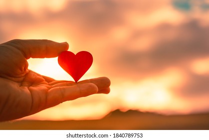 Abstract Closeup Of Red Heart In Hand On Beautiful Sunset Nature Background. Love And Compassion Concept. 