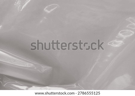 Abstract close-up of a translucent plastic surface with soft reflections and folds, creating a minimal monochrome textured background.