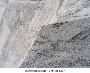 Abstract close-up view where two slabs of grey granite stone meet, showcasing the dramatic, contrasting dark and light flowing vein patterns across the surface. The scene represents premium architectural finishes, abstract natural art, and precise craftsmanship.