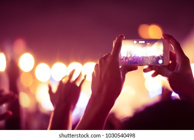 abstract colorful background of hand holding smart phone to taking memories by capture image photo and record video of lighting and people crowded in concert music event.using camera mobile concept.