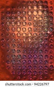 Abstract composition: close-up of textured bubble surface creates compelling visual effect with rich shades of deep orange, purple, and reflective metallic silver forming eye-catching aurora of warm tones. Circular bubbles arranged in grid-like pattern display rounded shapes that catch and distort illumination in various ways, generating playful interaction between luminance and structure. This effect adds depth and complexity to photograph, inviting exploration of intricate bubble details with soft, diffused lighting suggesting indoor setting. Gentle highlights enhance three-dimensional appearance of materials, creating dynamic composition emphasizing tactile quality that evokes curiosity and engagement. Suitable for commercial contexts including packaging design, product promotion in beauty or technology sectors, and background texture for digital or print media. Abstract nature supports versatile use in marketing materials emphasizing themes of innovation, modernity, and sensory experience.