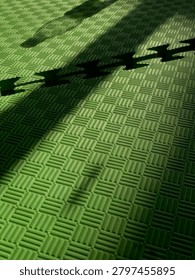Abstract composition of dramatic shadows cast over a green textured foam mat, creating a visually striking interplay of light, pattern, and depth