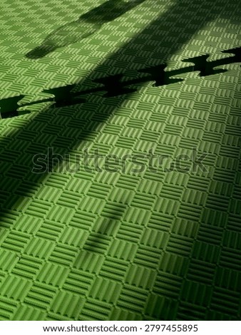 Abstract composition of dramatic shadows cast over a green textured foam mat, creating a visually striking interplay of light, pattern, and depth