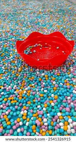 Abstract composition featuring a red toy constrasting with a bed of colourful porcelain sand. The porcelain sand is sensory play equipement in playground for kids