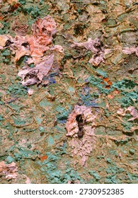 An abstract composition featuring scattered, thick paint fragments and smears in vibrant reds, yellows, blues, and purples resting on a textured greenish surface. The image evokes a sense of raw creativity, spontaneity, and the tactile beauty of dried pigments and layered brushstrokes.