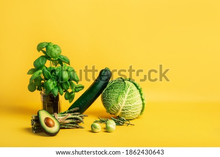 Abstract composition with fresh vegetables of cabbage, zucchini, asparagus, Brussels sprouts, avocado, basil on a yellow background. Vegetarian and vegan diet. Sustainable lifestyle, plantbased food.