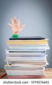 Abstract Concept Image Showing A Young Student Behind A Large Pile Of Test Prep Books On A Study Desk. An Overwhelming Load. The Kid Is Trying To Raise Hand. A Demanding Curriculum