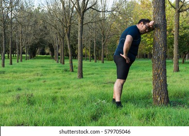 Abstract And Conceptual Tired, Tired Man In The Woods. Man Weighed Down, Resting After A Run In The Woods, Leaning Against A Tree.