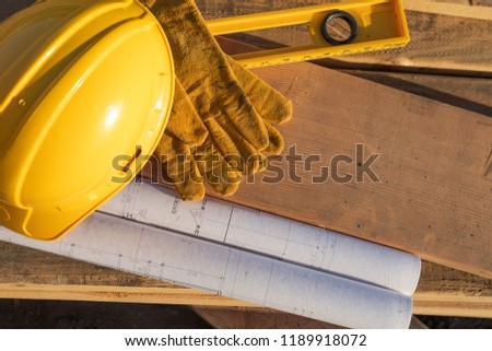 Abstract of Constrcution Hard Hat, Gloves, Level and House Plans Resting on Wood Planks.