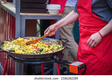 Abstract Cook In Red Apron Preparing Seafood Paella Outdoors. Picnic, Fest, Summer Concept