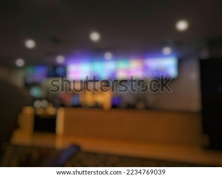 Abstract Dark Blurred effect image of ticket sale counter with silhouette of woman playing handphone at movie theater or cinema area.