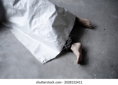abstract of dead body with bare foot was cover by white sack, lying on concret floor with desaturated tone. Abandon ed woman body die alone.